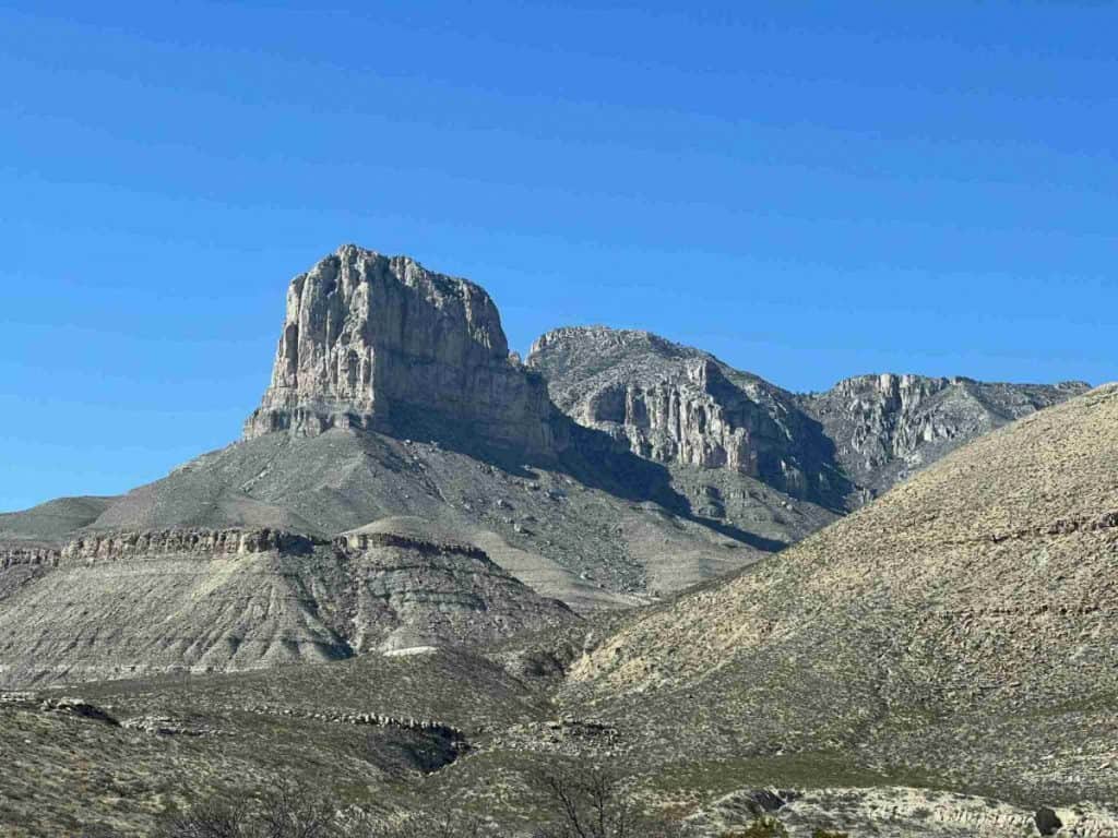 A pronounced peak dominates the horizon under a vast blue sky