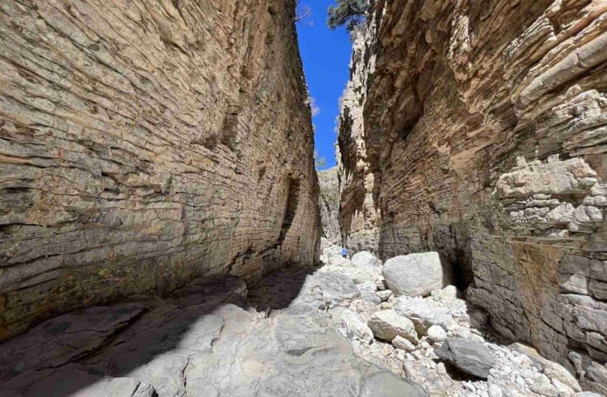 A woman stands between two towering, narrow canyon walls