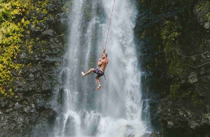 man hanging on rope near waterfalls during daytime