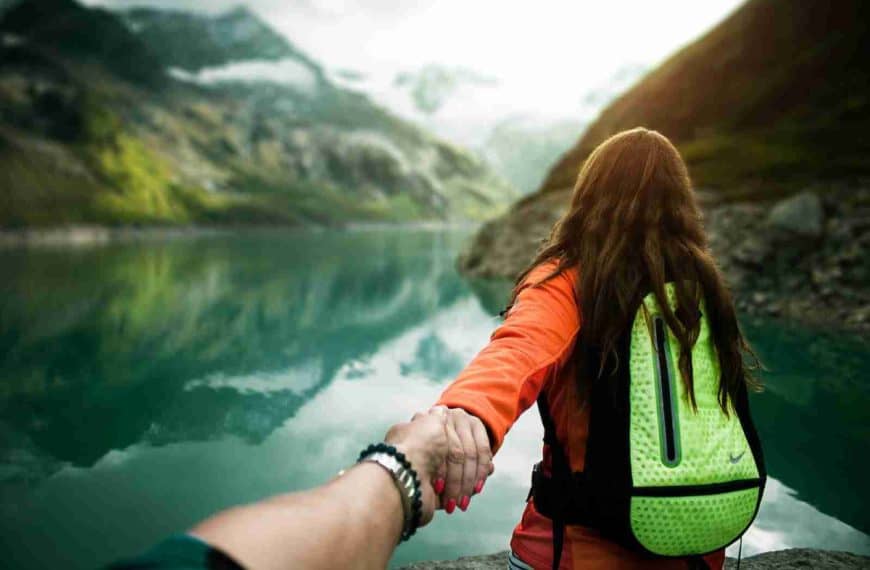 woman holding man's hand in front of water and mountains