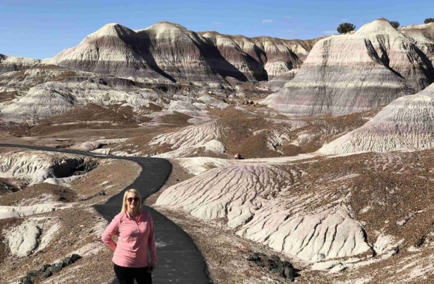 A woman stands on a paved path by colorful, striped mounds - Blue Mesa Trail in Petrified Forest National Park.