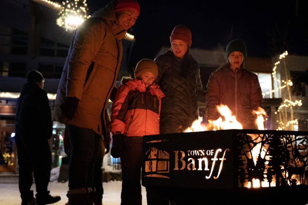 Guests warm up by huddling around a fire pit at night at the SnowDays Festival in Banff
