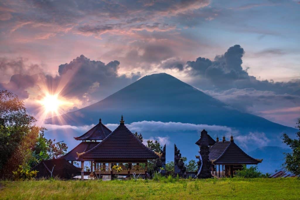 The sun sets over a volcano and temples in Bali.