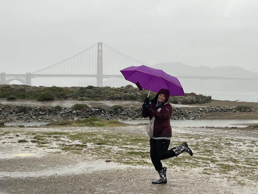 Julie McConkey of Miles with McConkey Travel Blog has her umbrella up in the rain near the Golden Gate Bridge.