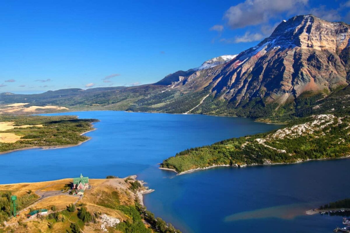 A cobalt blue lake glistens in the sun with a soaring mountain in the background
