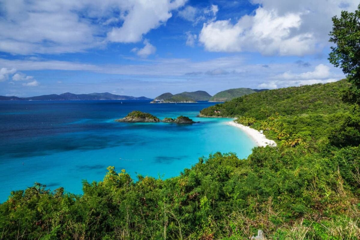 Green trees line the shores of a white sand beach with turquoise waters