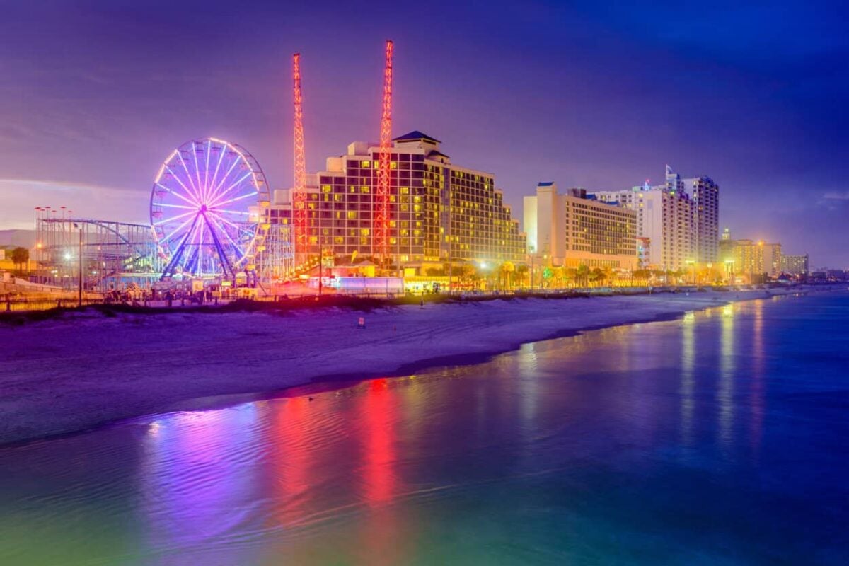 Lights shine on a ferris wheel and buildings on Daytona Beach at nightfall