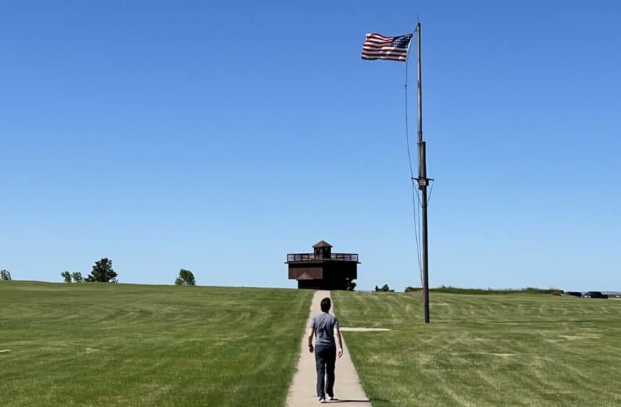 A man walks toward a blockhouse in Fort Abraham Lincoln State Park as the American flag flies on a pole ahead