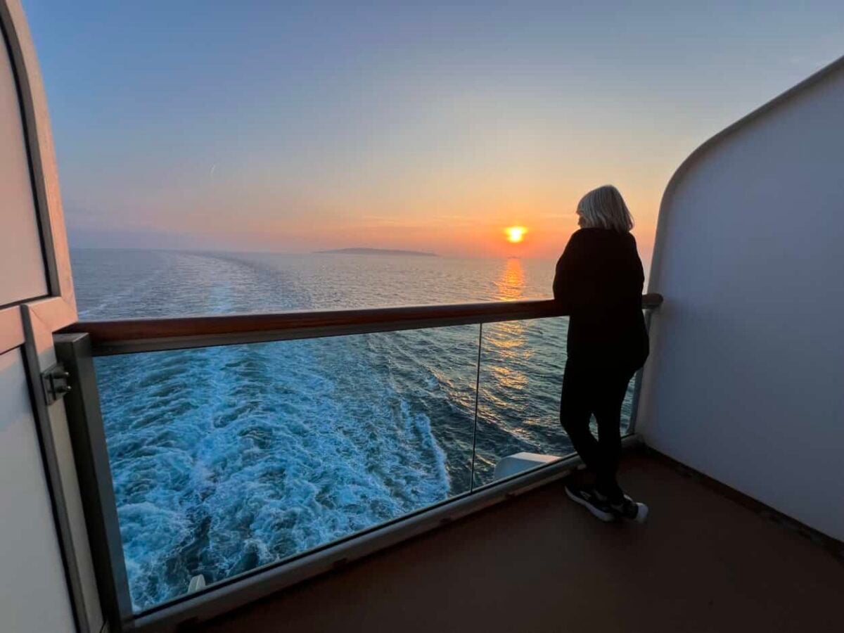 A woman watches sunset from her cruise ship balcony