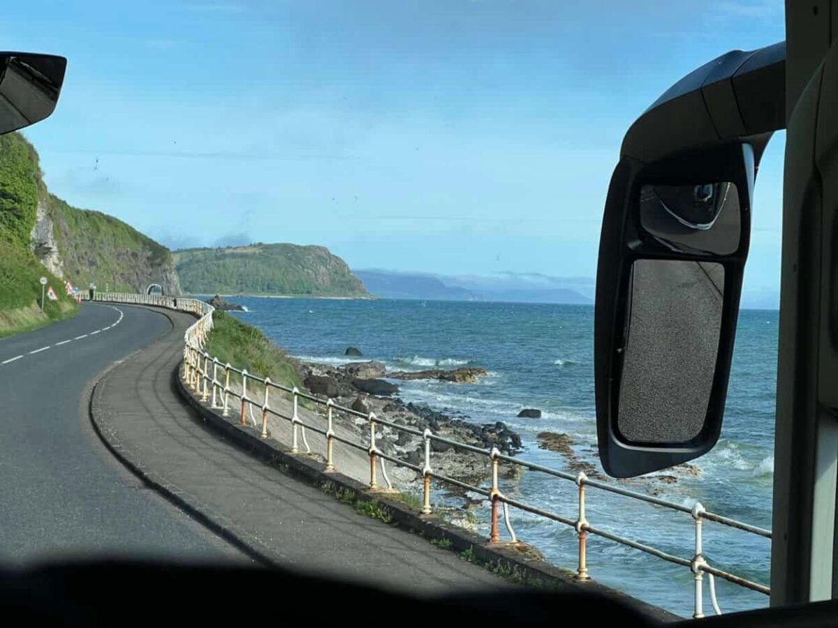 A bus drives along the Northern Ireland coast as waves gently roll ashore