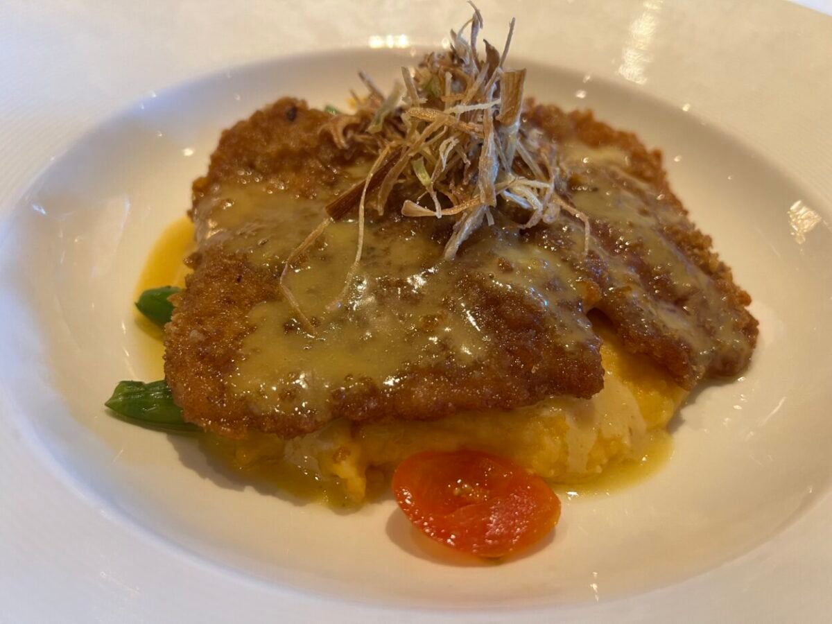 A plate of fried turkey atop potatoes with cheese and a tomato slice.