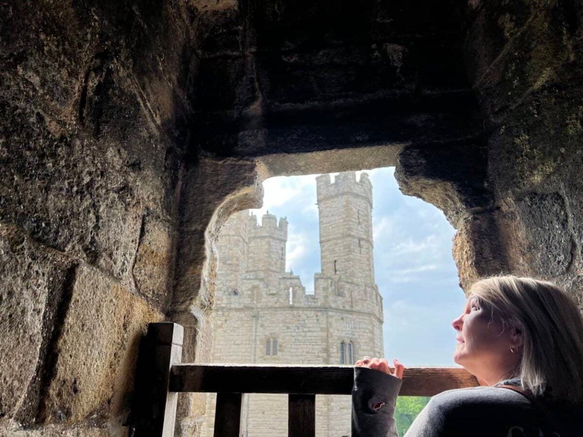 A woman looks at a castle from a stone window