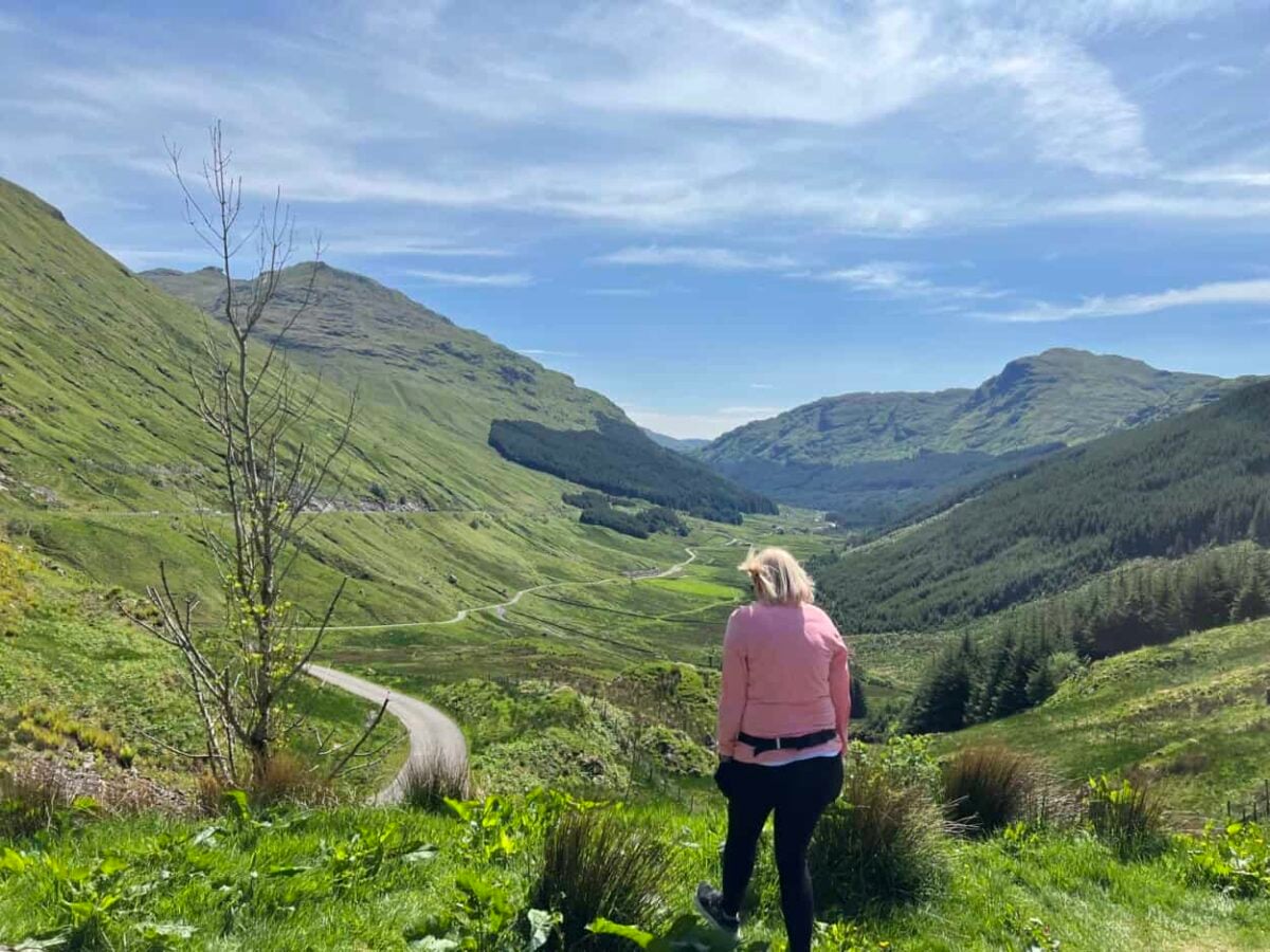 A woman walks through a valley surrounded by lush green mountains
