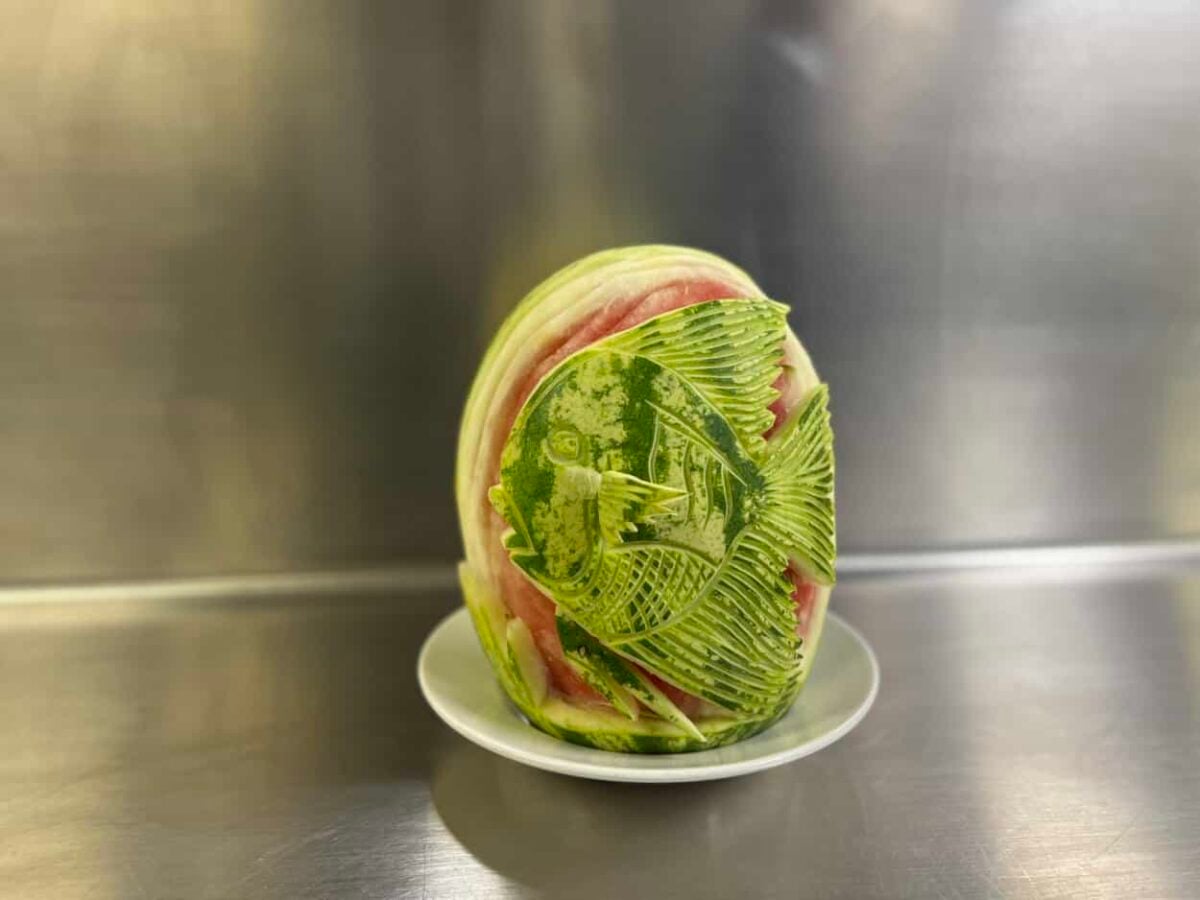 A carved watermelon depicting a fish sits on a white ceramic plate