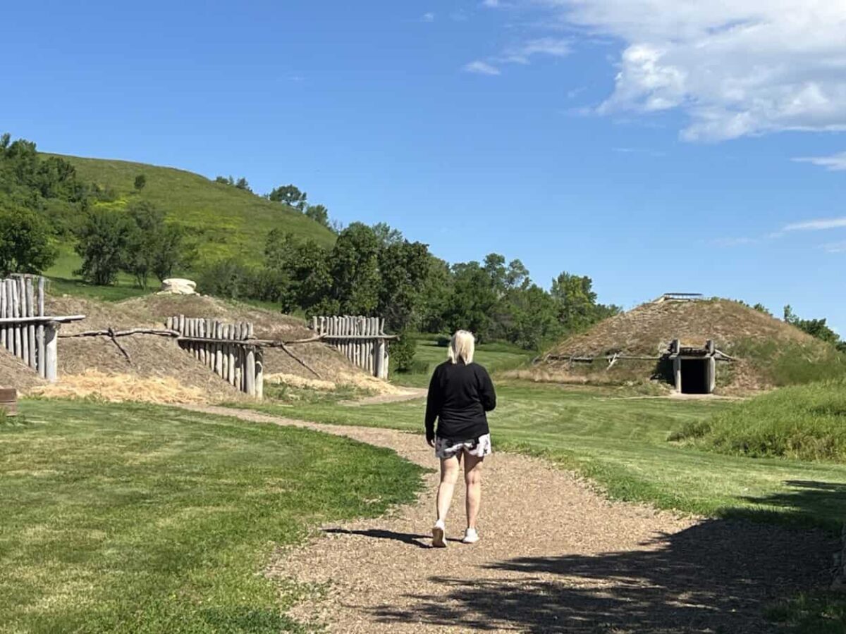A woman walks along a path with earth lodges