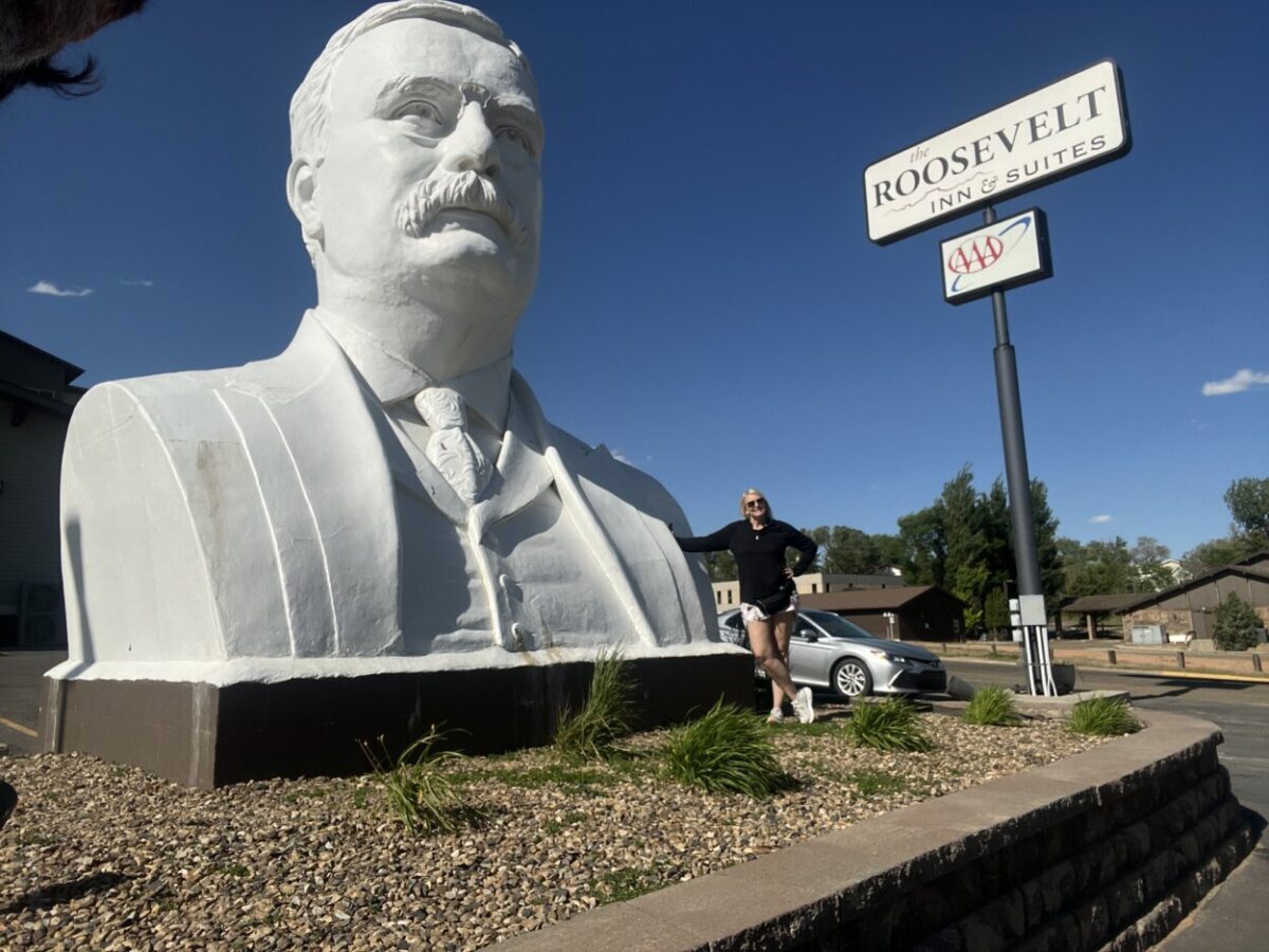A woman poses for a picture in front of a giant Theodore Roosevelt bust.