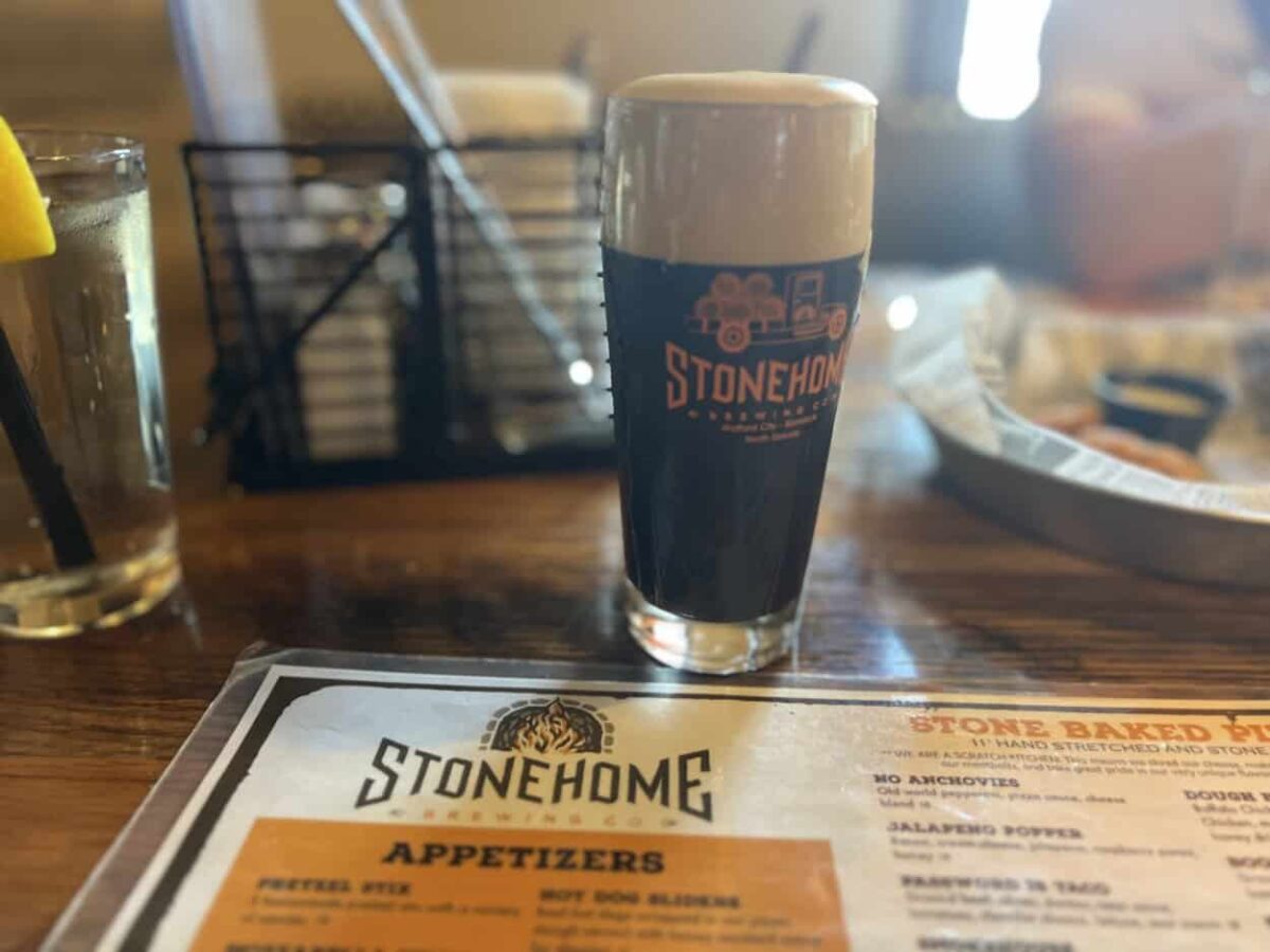 A glass of dark beer with a foamy head sits on a table