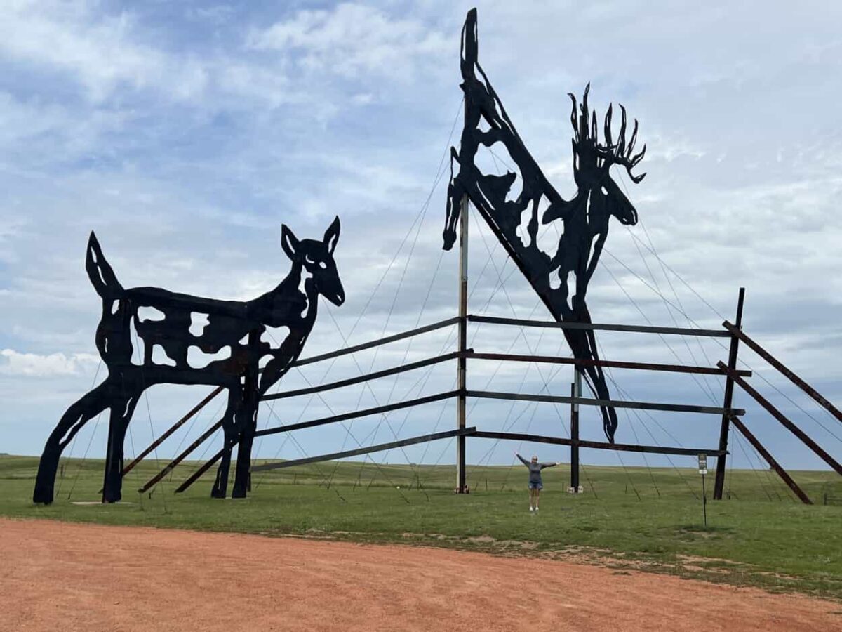 Giant roadside sculpture with deer jumping a fence