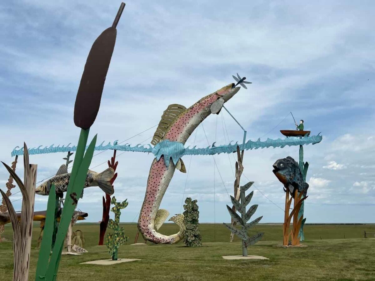 A metal sculpture with cattails, seaweed, fish, and a man fishing from a small boat