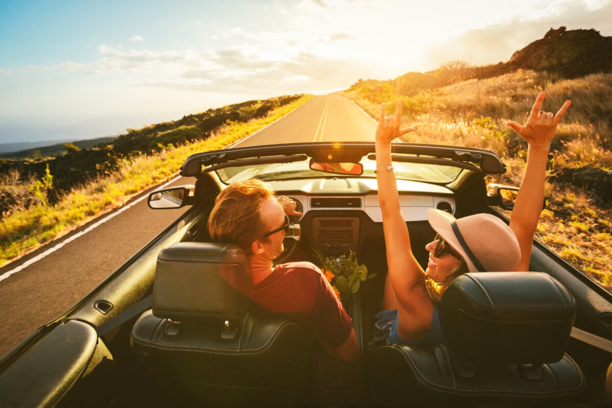 A happy young carefree couple drive along a country road.