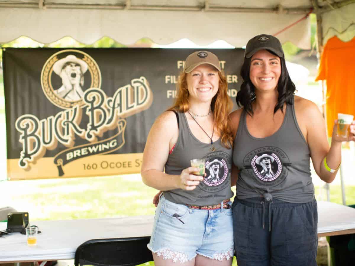 Two women smile for a picture while each holding a cup of beer