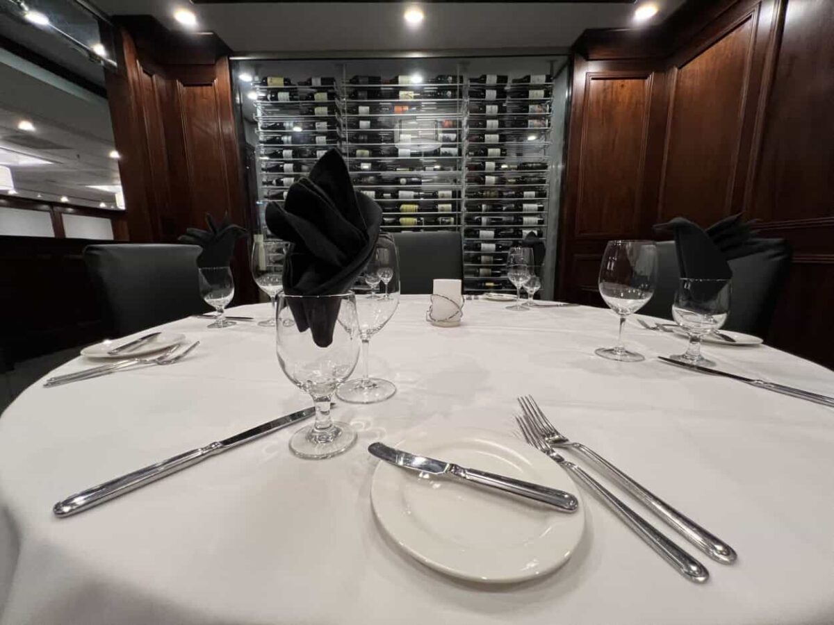 A case filled with bottles of wine sits behind a table set for dinner.