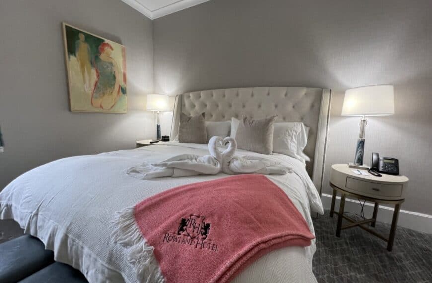 Towels folded in the shape of swans sit on a hotel room bed