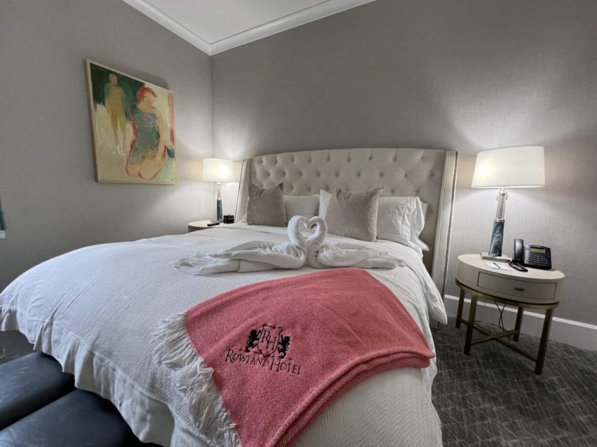 Towels folded in the shape of swans sit on a hotel room bed