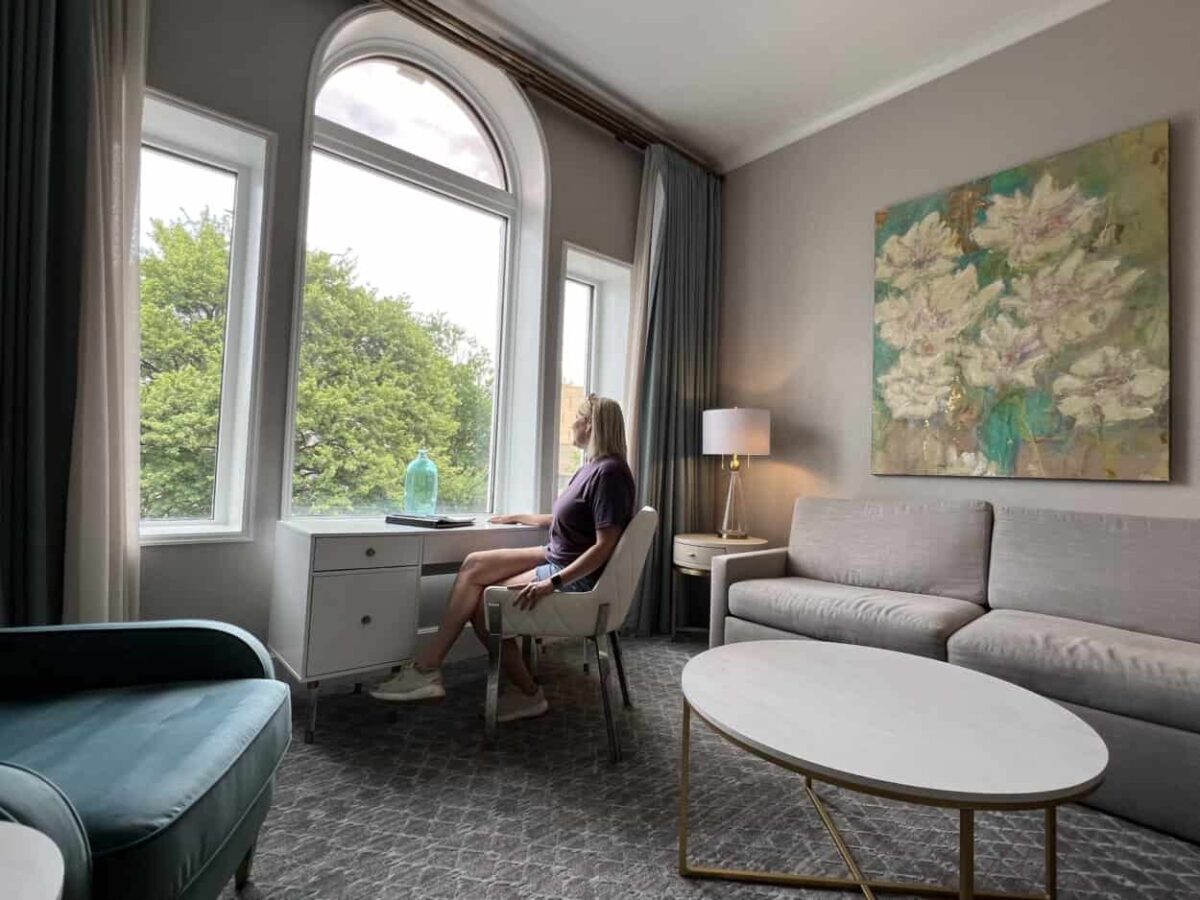 A woman sits at a desk in her hotel room and looks out the window