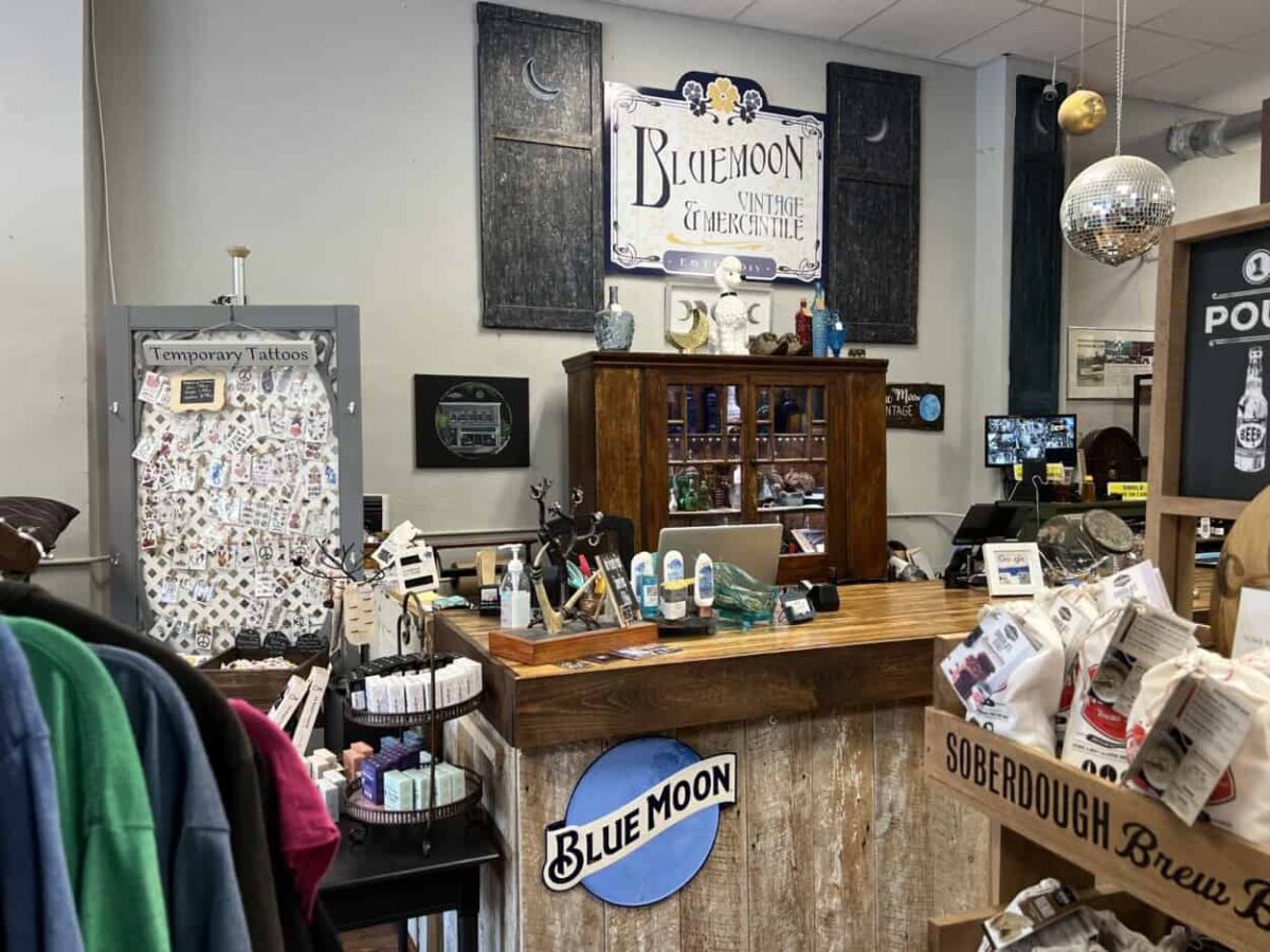 A sign that says Blue Moon is attached to the side of a counter in a store with assorted goods