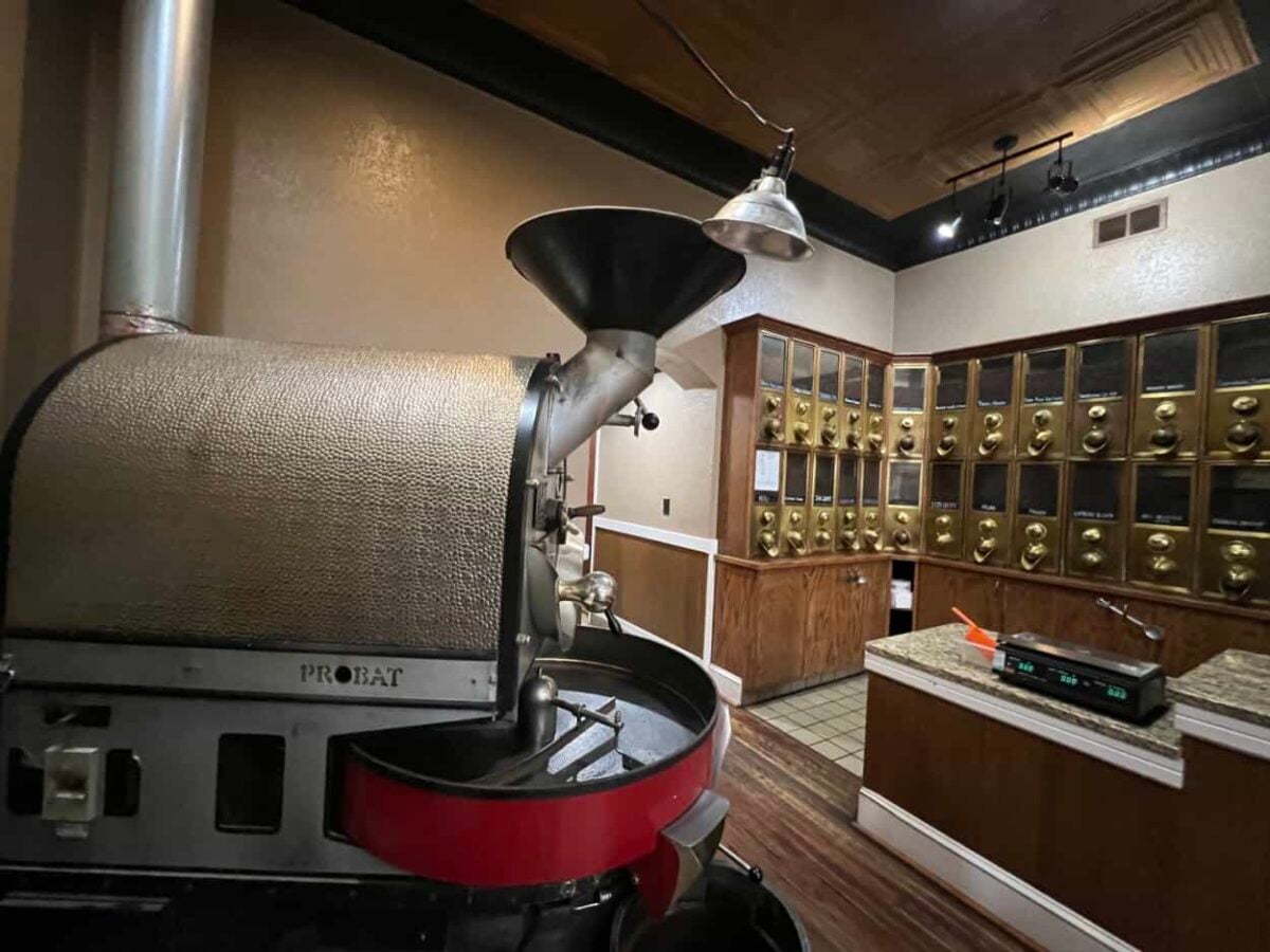 A coffee grinder with vaults of different coffee beans in the background