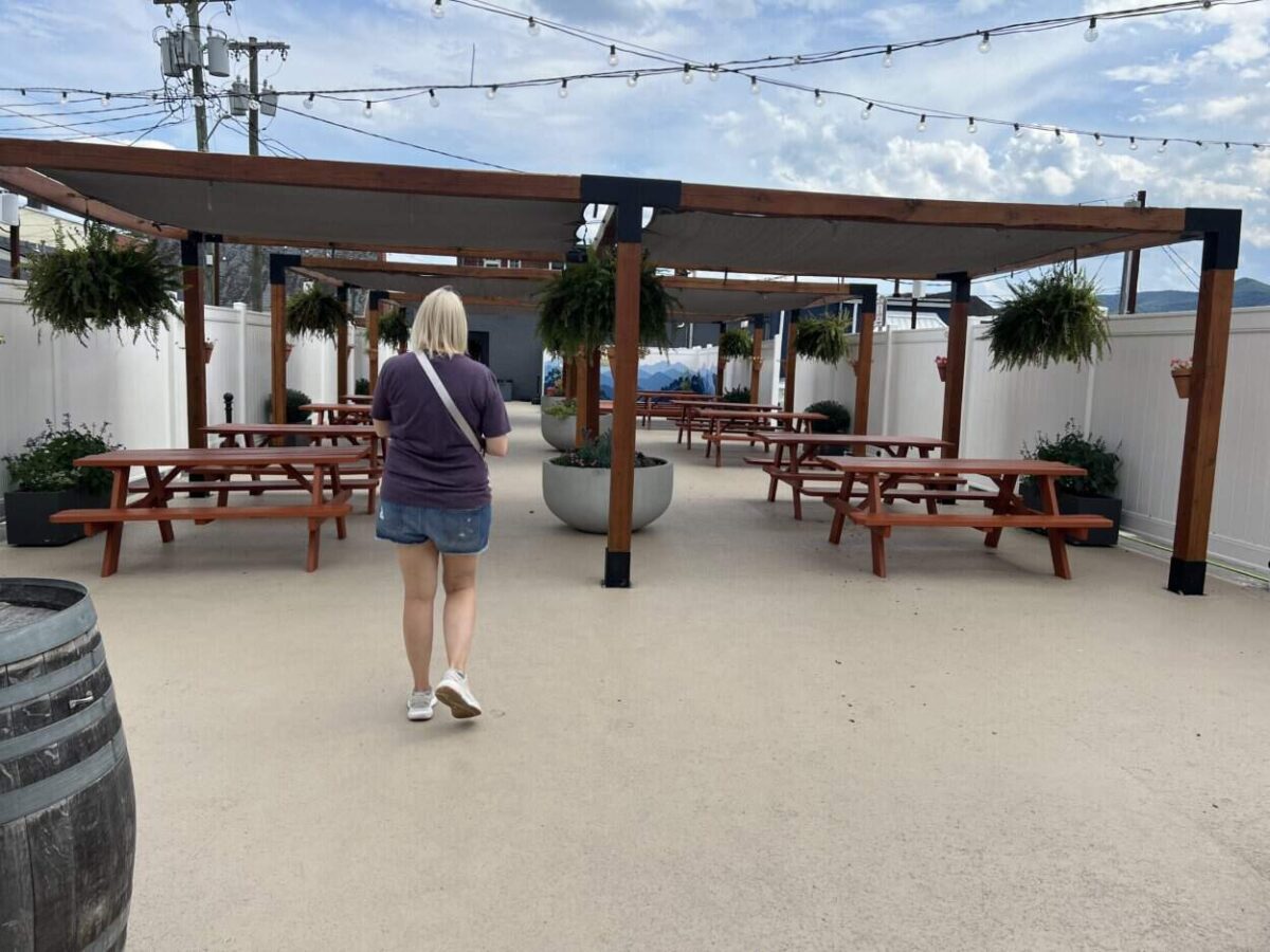 A woman walk toward outdoor picnic tables under a canopy and string lights