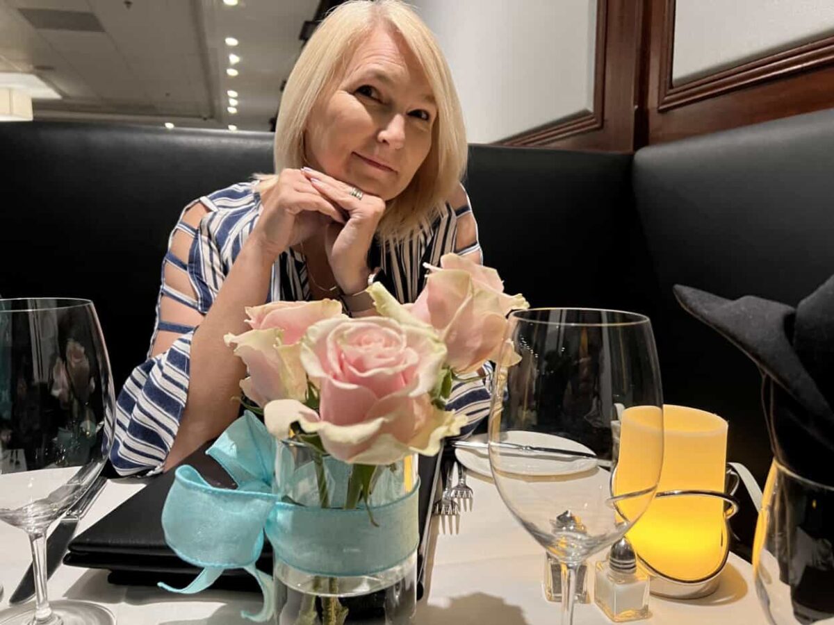 A woman sits at an elegant dinner table decorated with a vase of roses and a lit candle