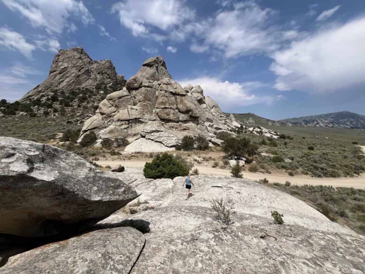 A woman walks down a massive rock with other giant rock formations looming in the background