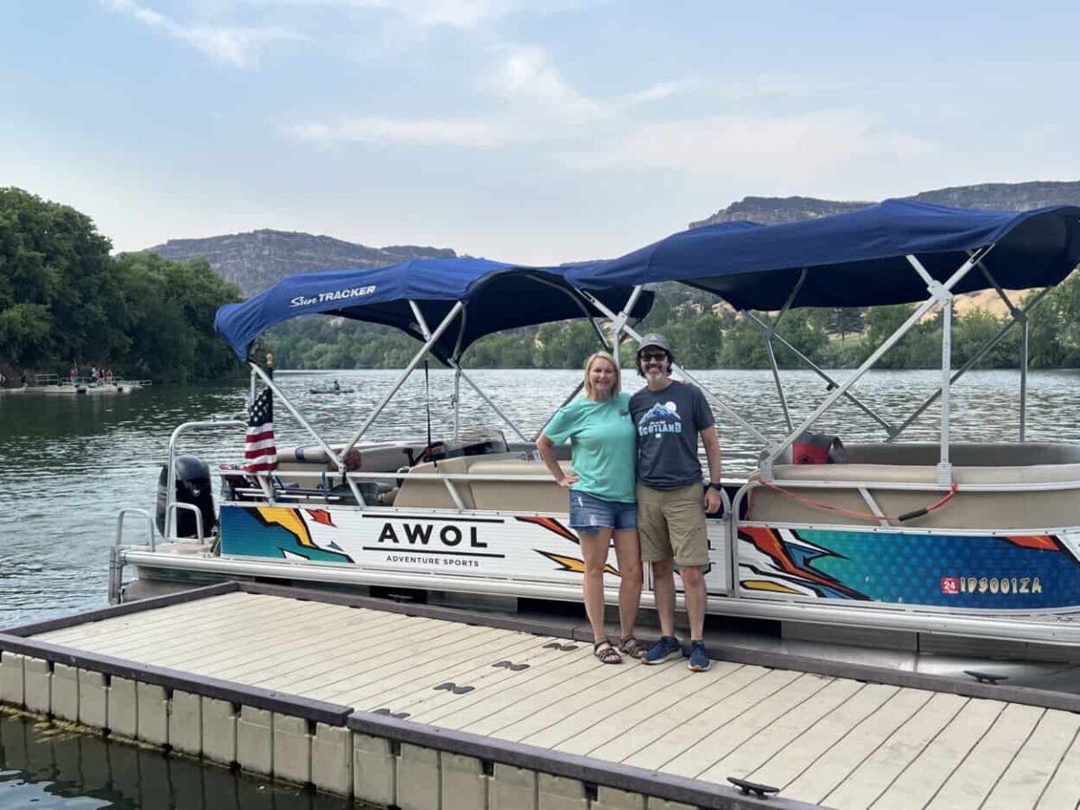 Scott McConkey and Julie McConkey of the Miles with McConkey Travel Blog pose for a picture in front of a boat along the Snake River in southern Idaho.