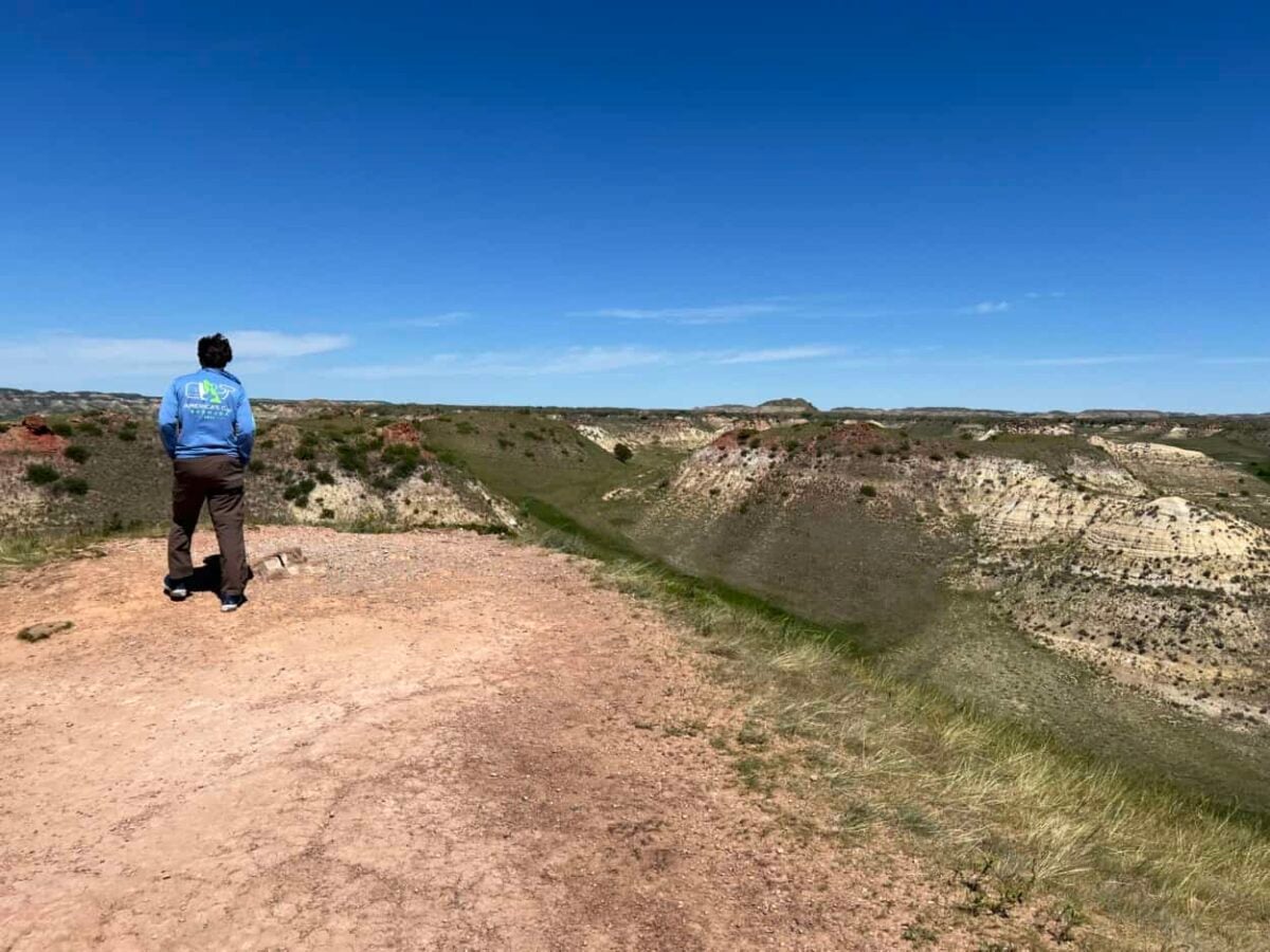 A man walks along a red clay path to get a closer view of colorful badlands