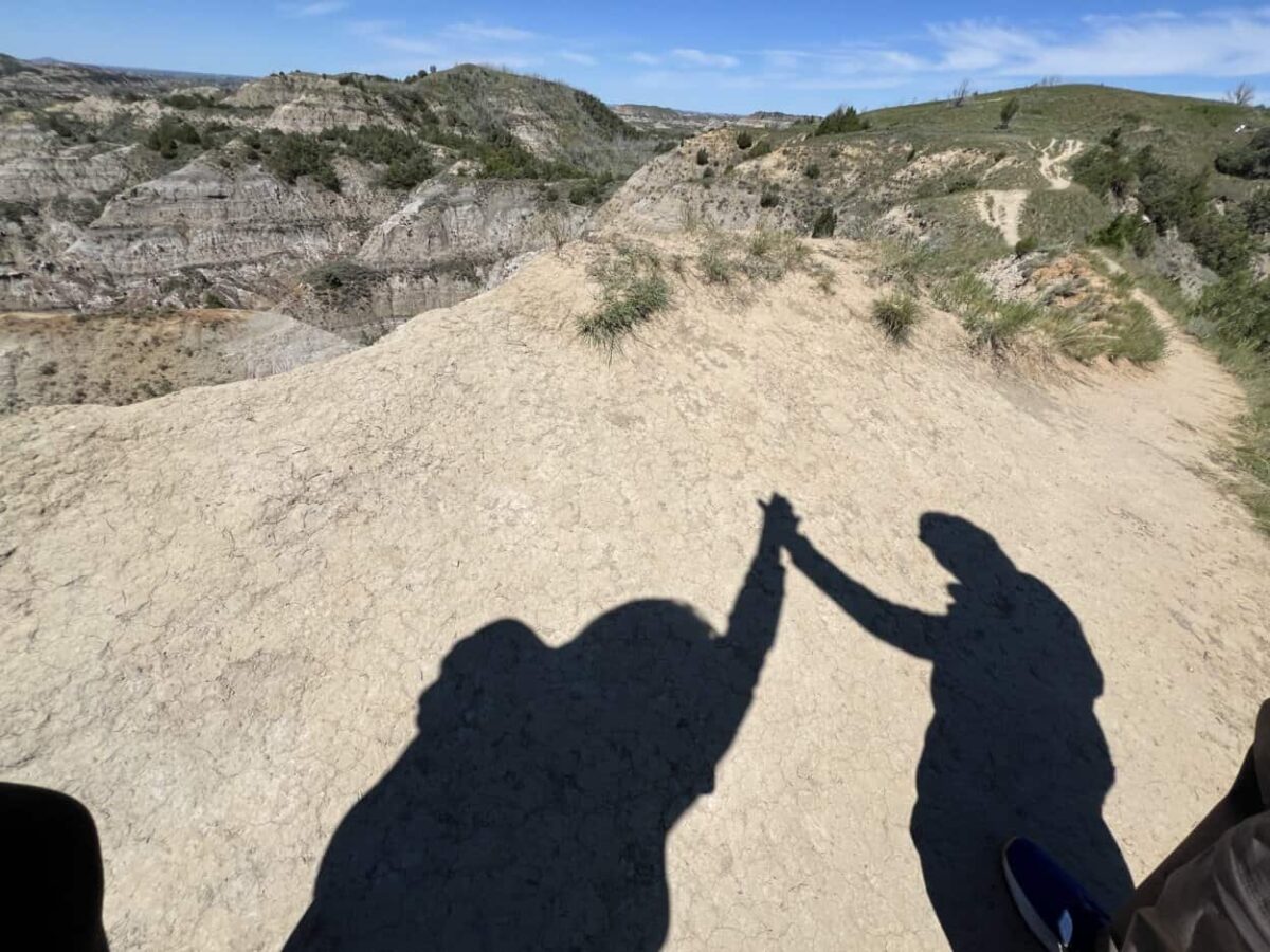 Shadows show tow people giving a high five with badlands in the background