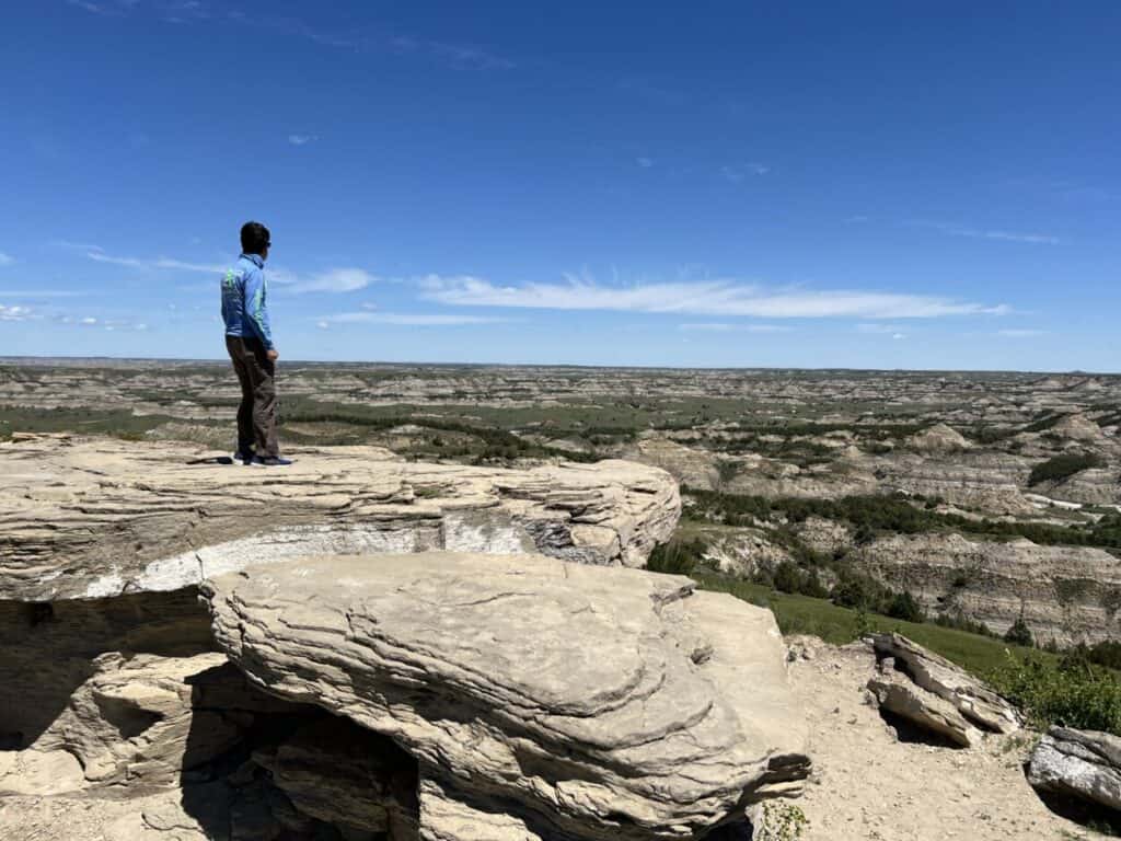 Scott McConkey, travel writer and founder of the Miles with McConkey Travel Blog, stands on a rocky platform overlooking badlands in Theodore Roosevelt National Park, ND
