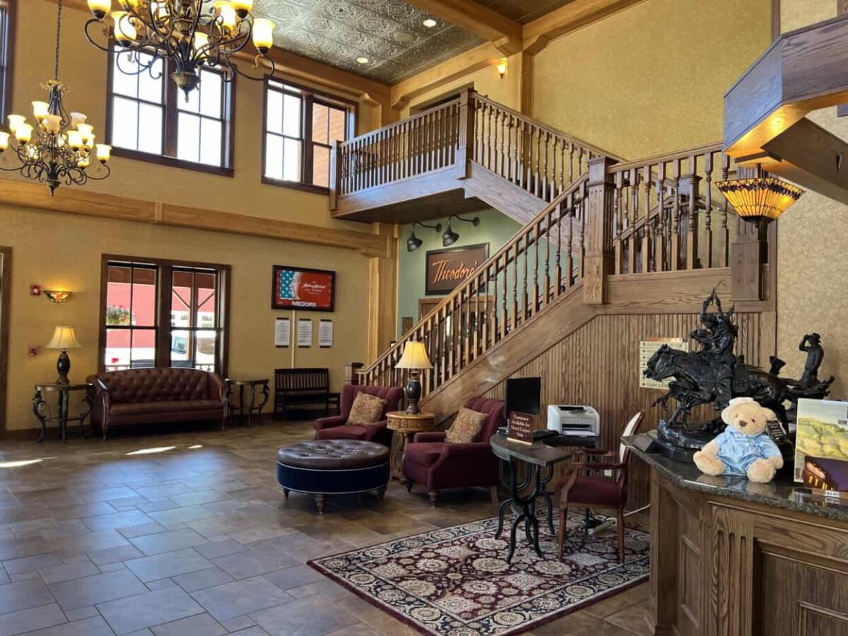 A stuffed teddy bear and a small statue of Theodore Roosevelt riding a horse sit on the desk in a hotel lobby