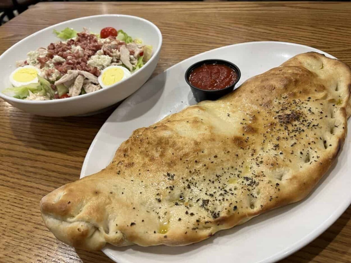 A bowl of salad and a plate with a large calzone sit on a table