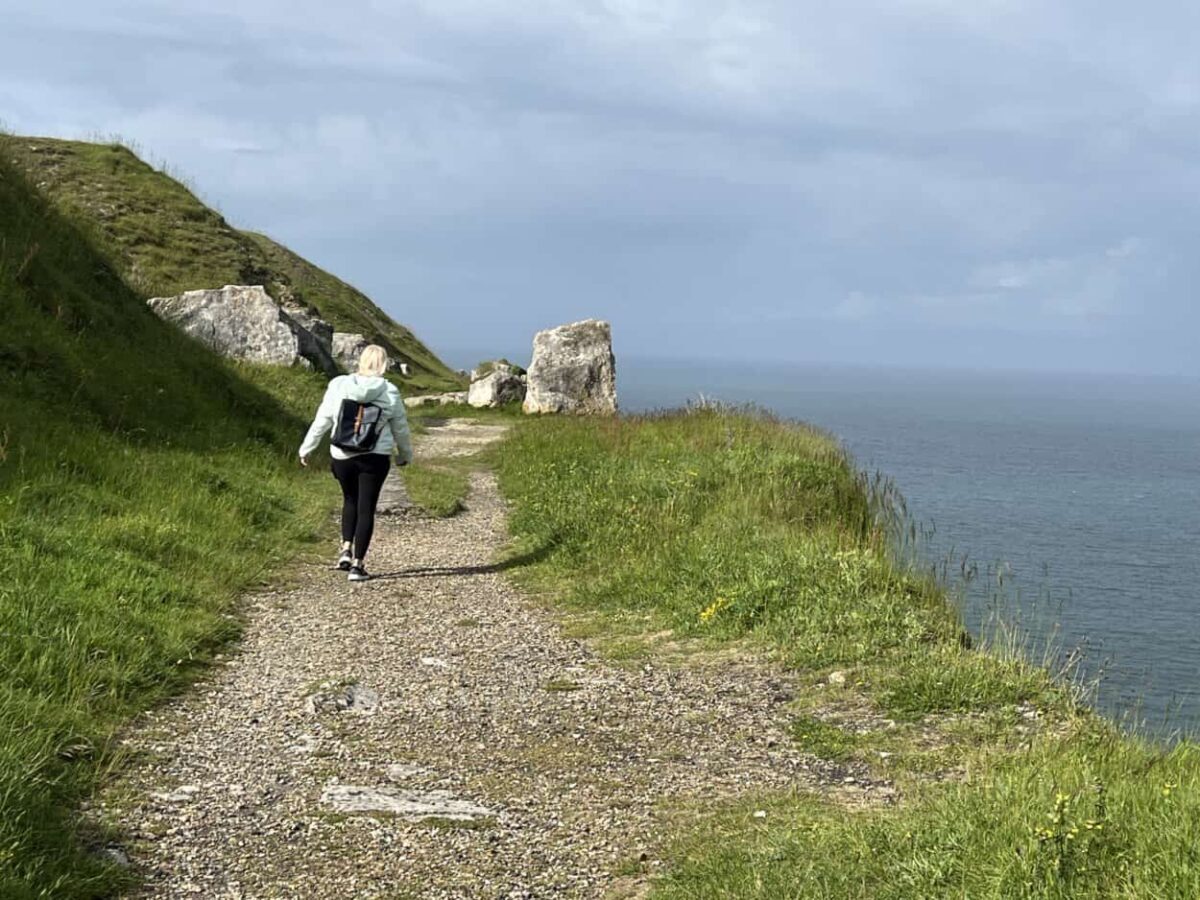 A woman hikes a trail along a cliff overlooking water below