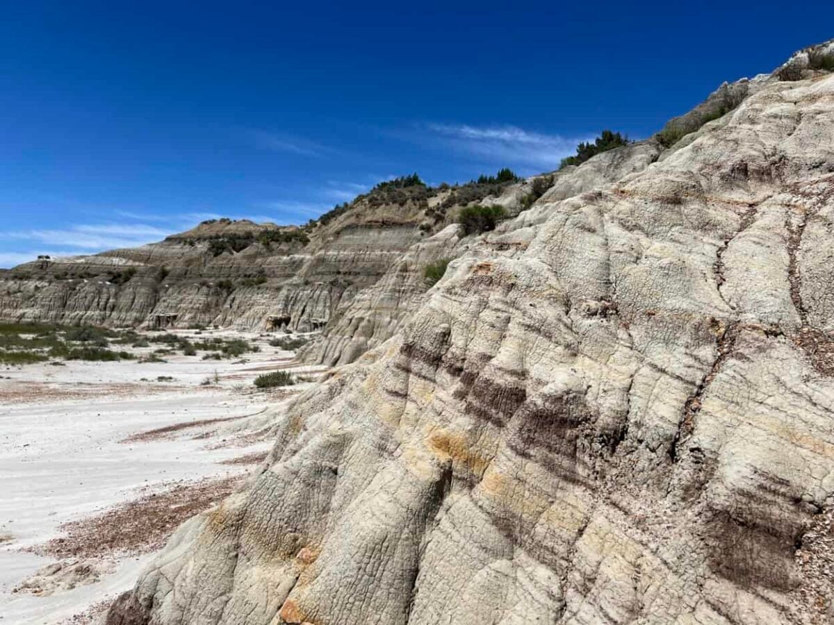Colorful stripes stand out on badlands against white sand and blue skies