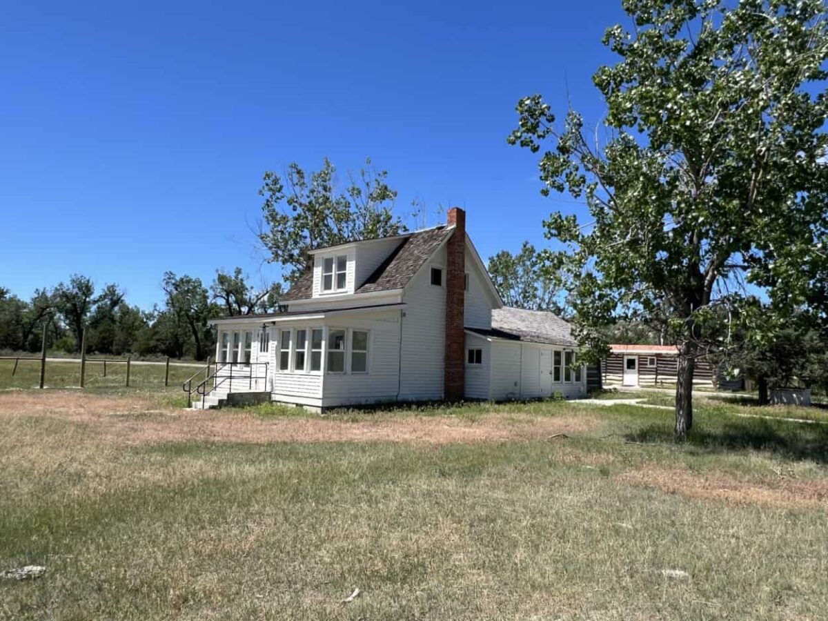 A white House in a grass field with trees