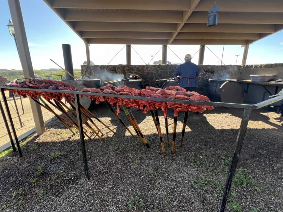 Pitchforks holding steaks are leaned against a rail and ready to be cooked by a chef in the background
