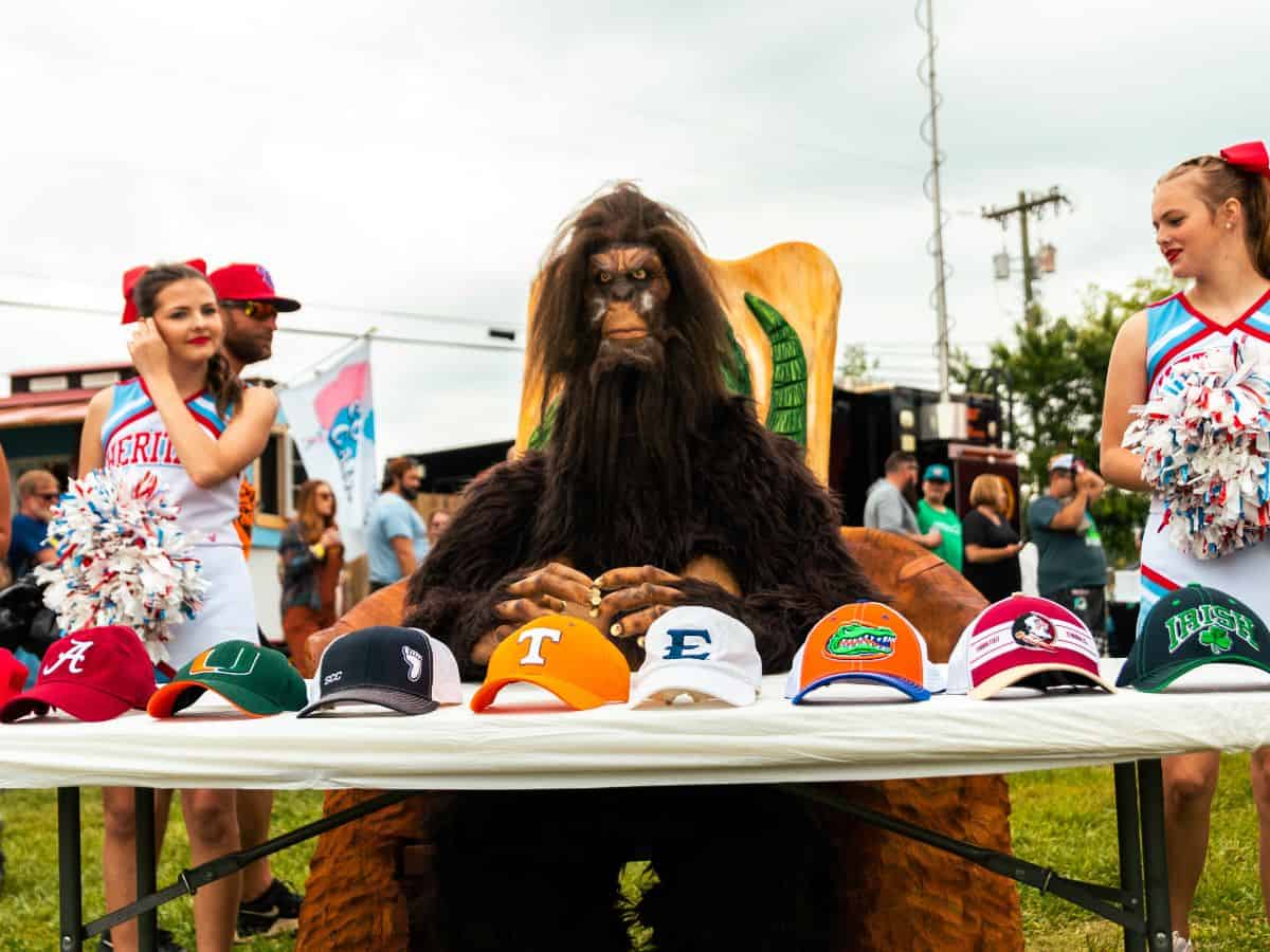 Two cheerleaders skeptically look at someone dressed as Bigfoot.