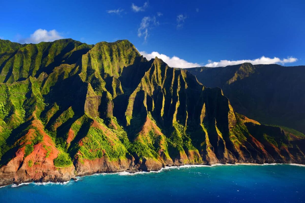 Blue waters lap against the shore of narrow green and red canyons