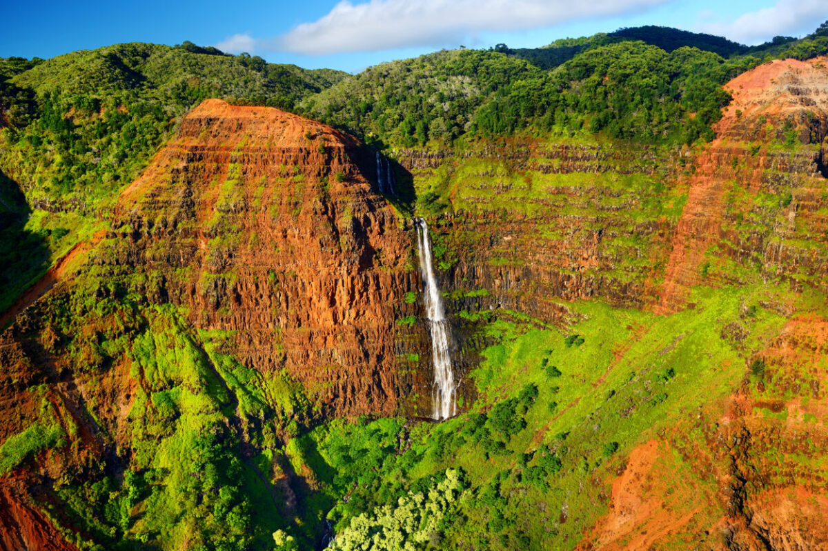 A waterfall flows from a green and red mountain
