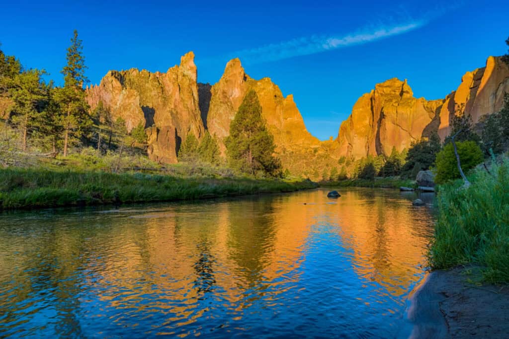 The sun shines brightly on large rocky spires by a lake