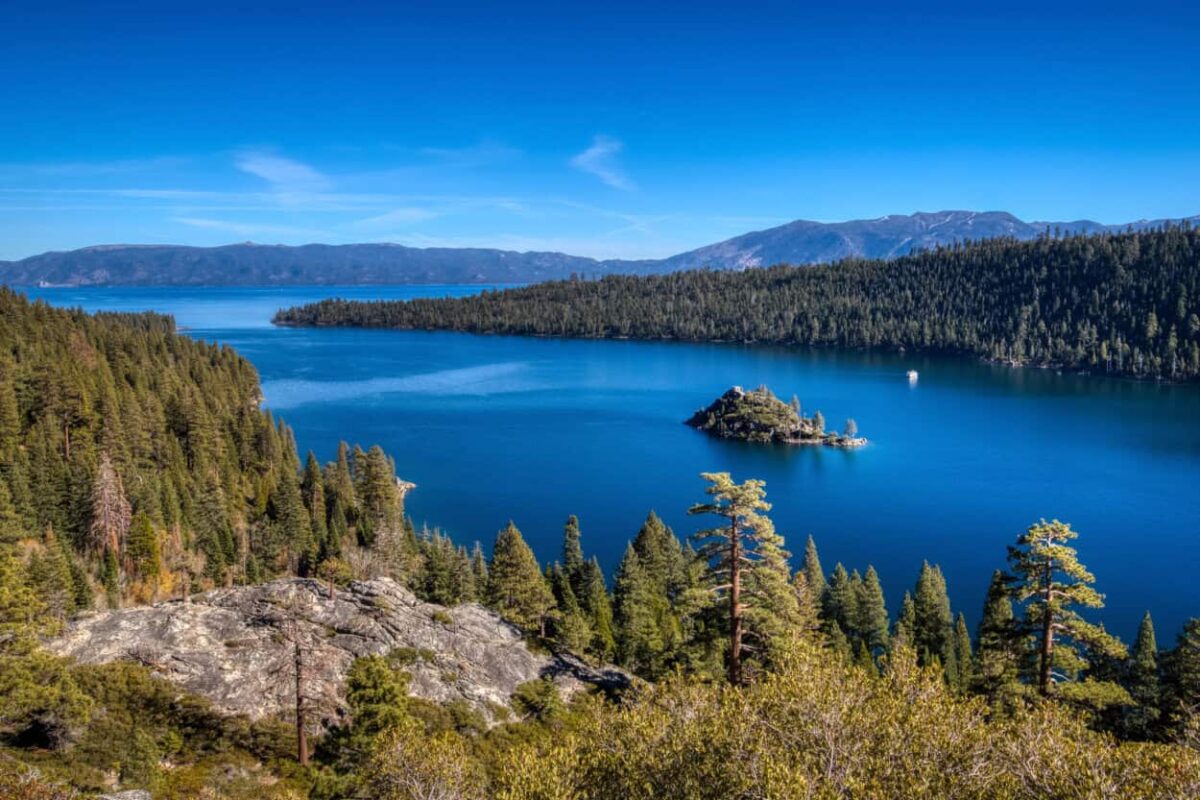 A small island sits in a bay with blue water and mountains in the background