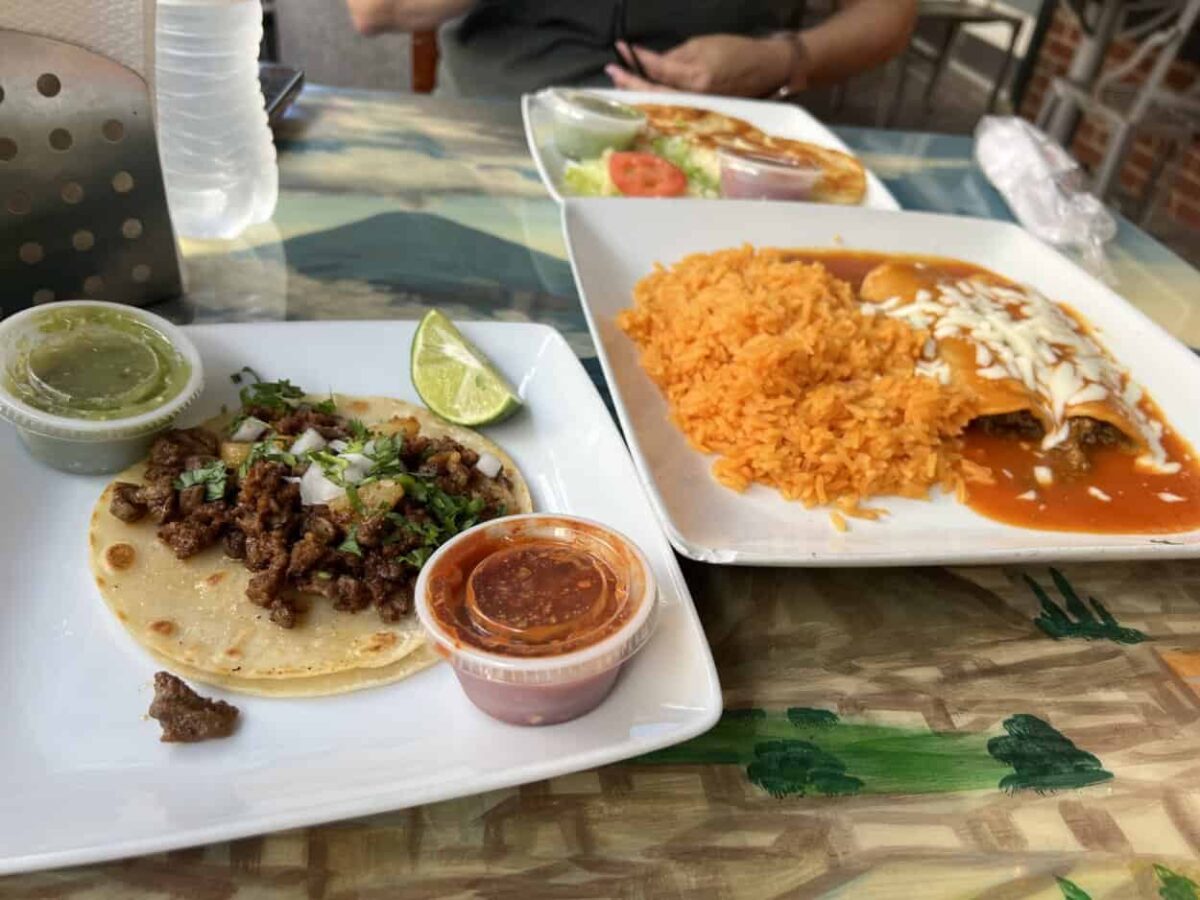 Three plates of Mexican food sit on a colorful table.